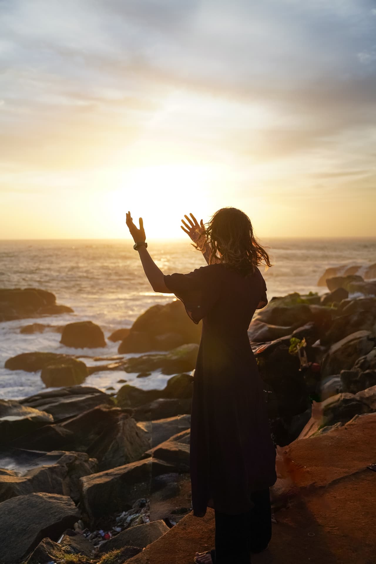 Silhouette raising hands towards a coastal sunset